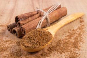Powdery cinnamon on wooden spoon and tied cinnamon sticks on wooden table seasoning for cooking and baking